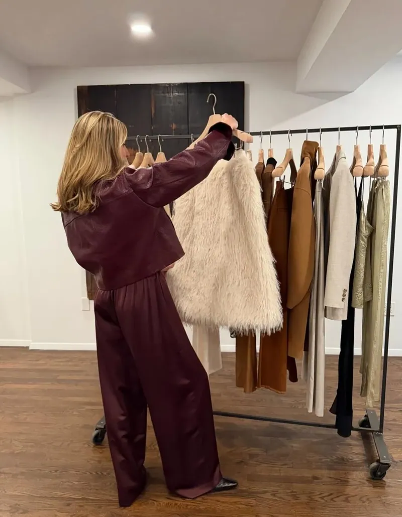 Annie in burgundy leather pulling a shaggy cream coat from a clothing rack
