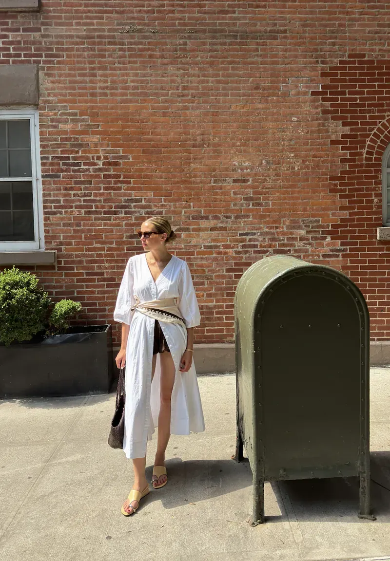 Annie in a white dress by a brick wall and a mailbox