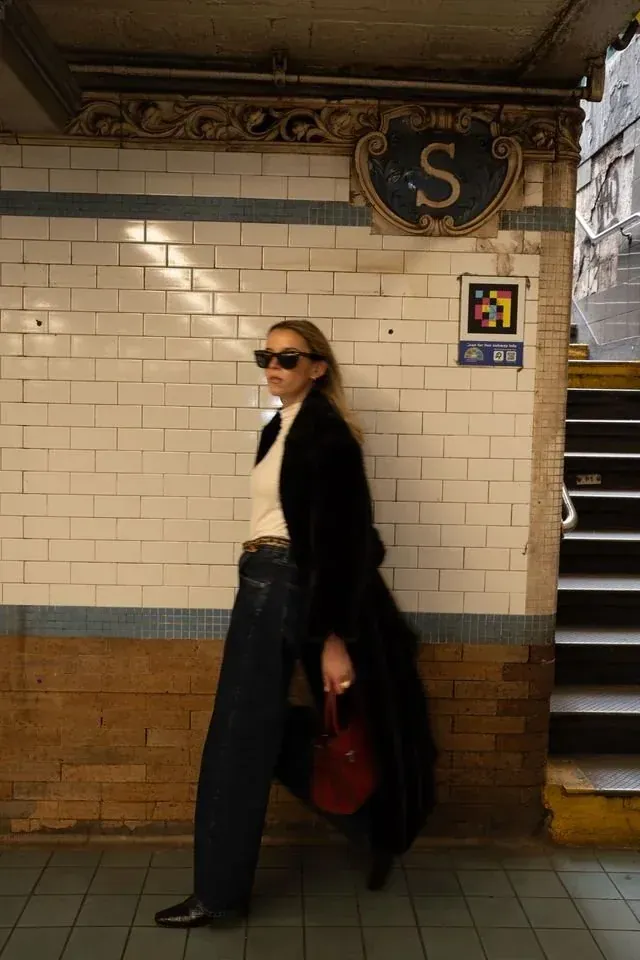 Annie on a subway platform in a black coat